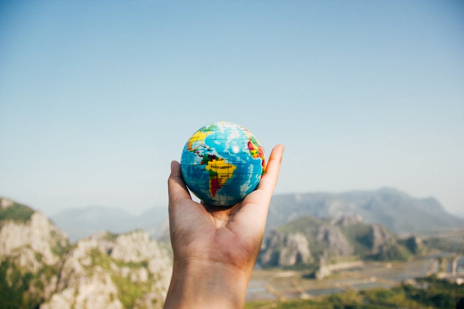 Hand holding a globe against a mountain background symbolizing travel and exploration